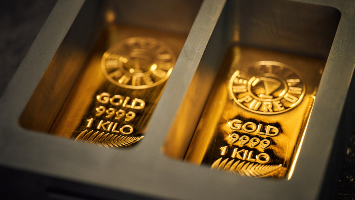 Two New Zealand Pure gold bars, each weighing 1 kilogram and stamped with "GOLD 9999" and a silver fern motif, resting in a mould.